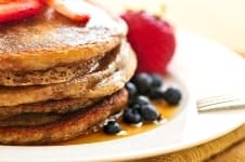 Stack of buckwheat pancakes with fresh berries and maple syrup