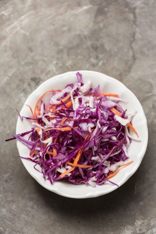 Red Cabbage Slaw Thinly sliced red cabbage, carrots and shallots in a white bowl on a concrete suface.