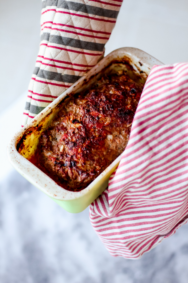 Hot Melt Meatloaf two hands in oven mitts holding a stoneware loaf pan of meatloaf