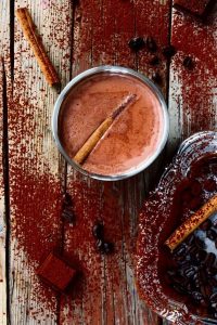 hot chocoate in a much with a cinnamon stick on a heavily cocoa-dusted wooden surface