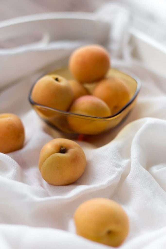 Peaches in a bowl and a few loose on a draped white cloth surface