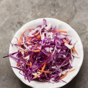 Thinly sliced red cabbage, carrots and shallots in a white bowl on a concrete suface.