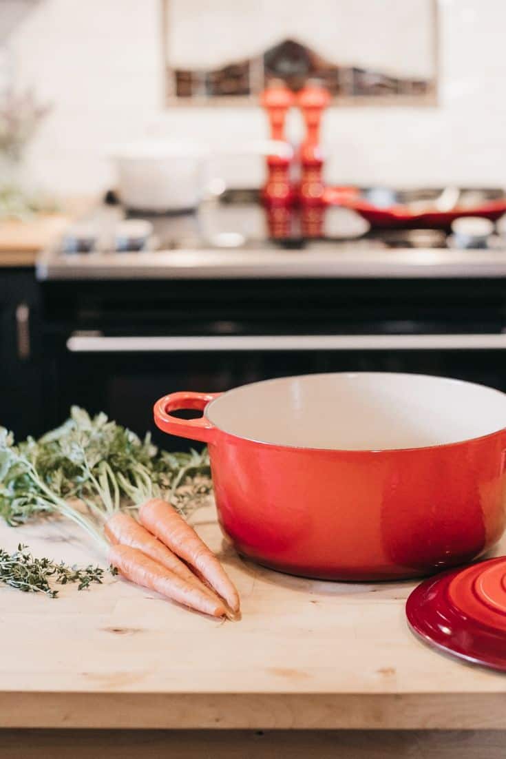 orange enameled stock pot on a wooden surface next to carrots and rosemary